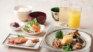 A table with various dishes, including sushi, a salad, and a bowl of rice. There are also two glasses of a yellow beverage and a green cup.