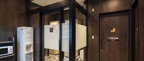 A modern hotel restroom with a self-service ice dispenser, a multi-function toilet, and a marble-tiled floor.