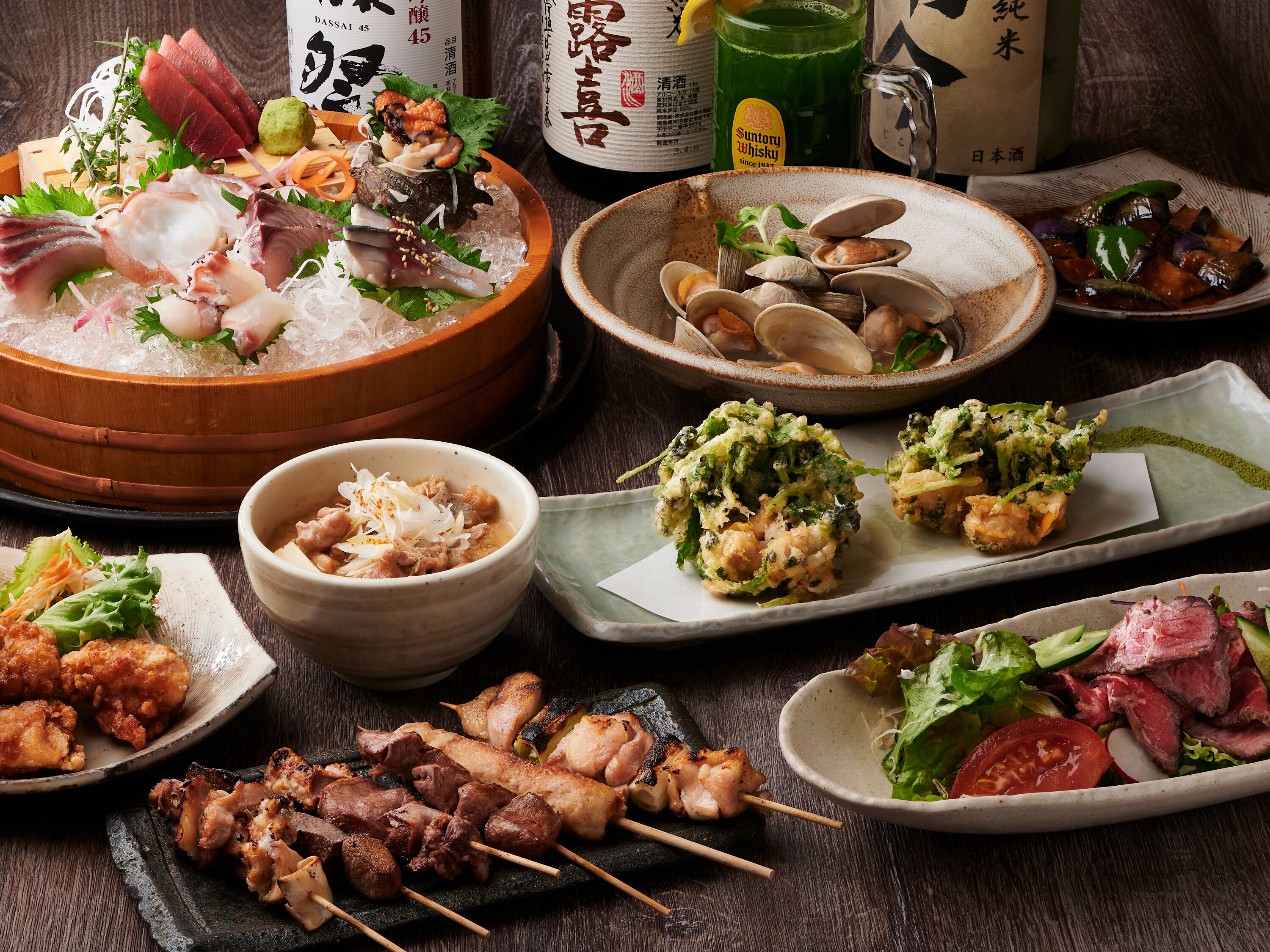 A variety of Japanese dishes including sashimi, grilled meat, and vegetables, served on a wooden table.