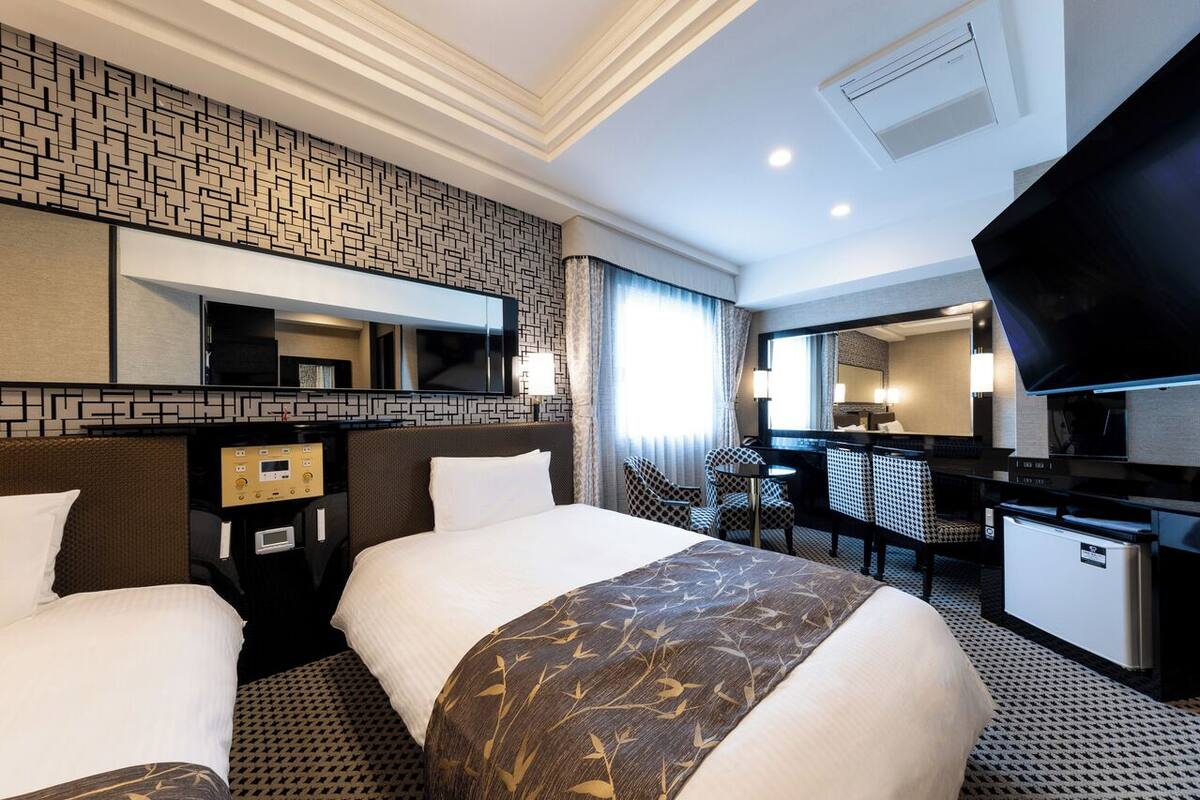 A hotel room with two beds, a desk, a TV, and a minibar.