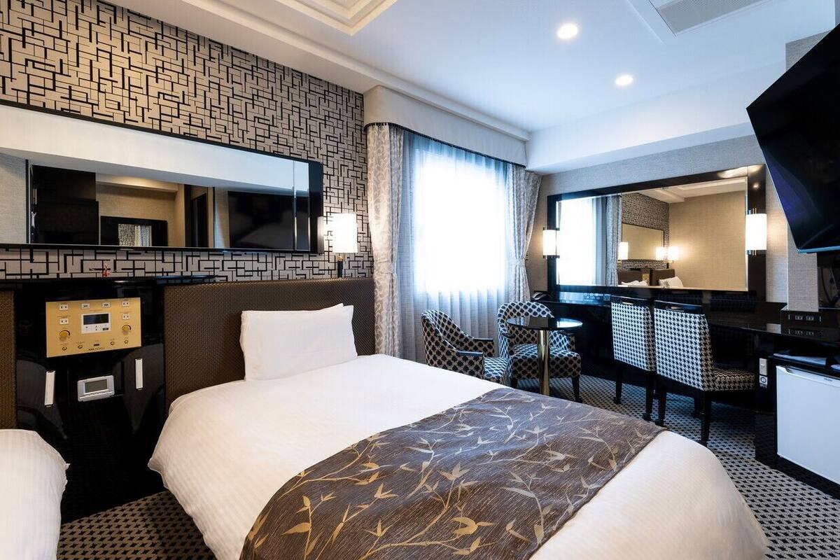 A hotel room with a bed, a desk, a chair, a TV, and a minibar.