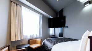 A hotel room with a bed, a chair, a small table, a TV mounted on the wall, and a window with curtains. - APA Hotel Chibachuo Ekimae (Chiba)