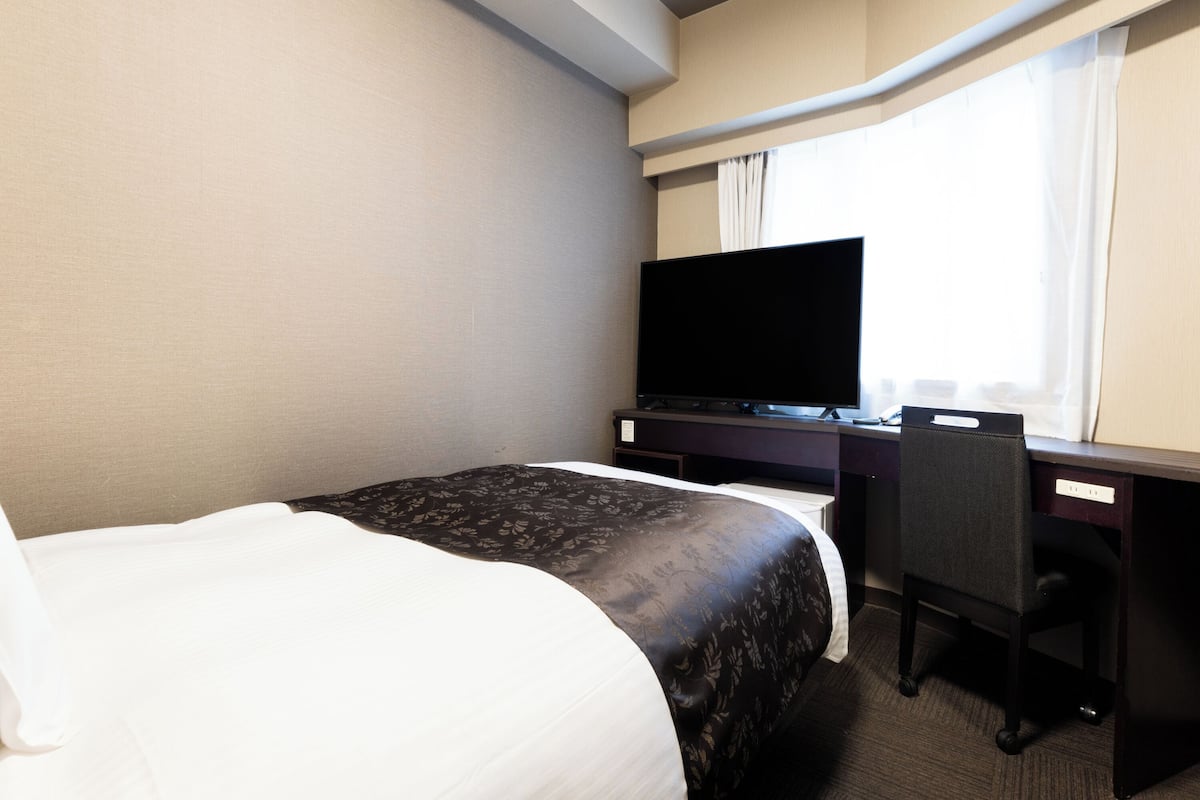 Quarto de hotel com cama, secretária com televisão e uma cadeira.