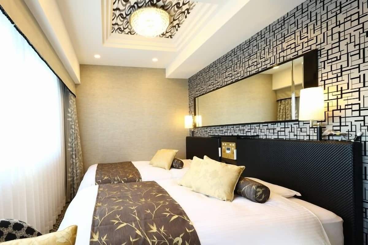 Una habitación de hotel con una cama grande, cabecera con diseño geométrico, un espejo amplio y una ventana con cortinas.