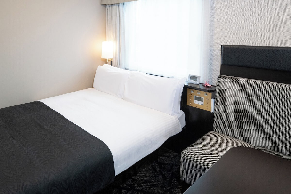 A hotel room with a bed, a bedside table with a lamp, and a headboard.