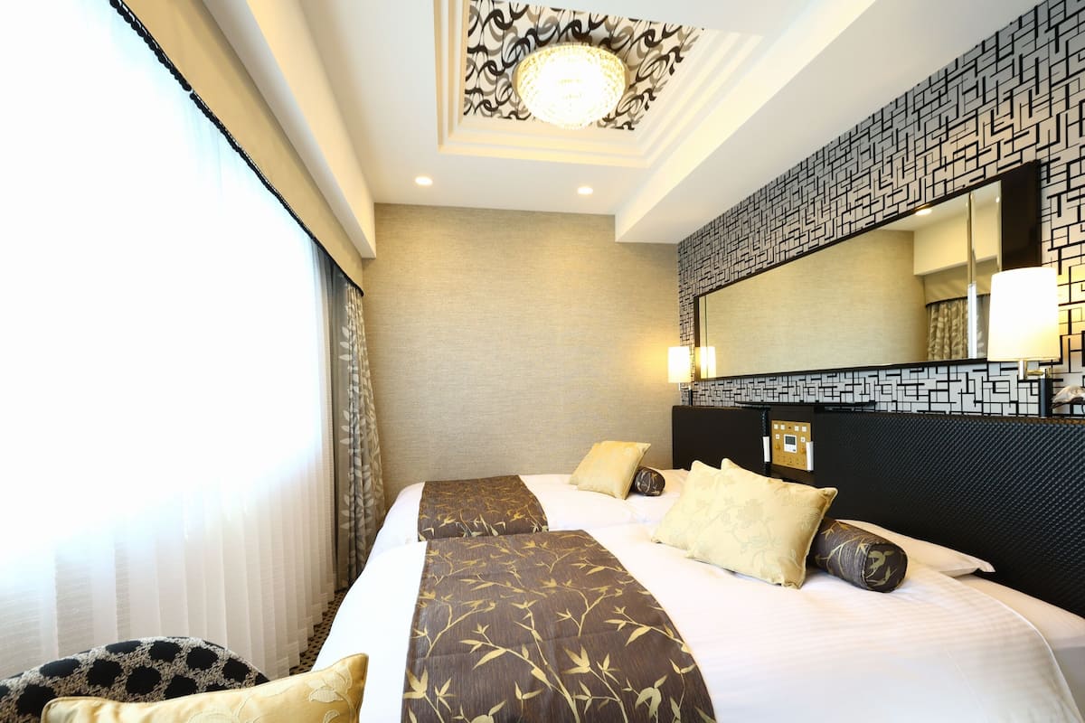 A hotel room with a large bed, two pillows, a headboard with a geometric pattern, a wall-mounted mirror, and a ceiling light fixture.