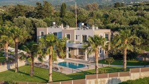 Une villa moderne dotée d’une piscine, entourée de palmiers et d’une pelouse bien entretenue.