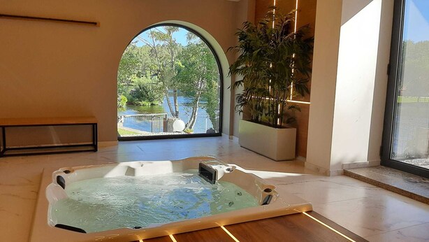 Une salle de spa équipée d’un bain à remous, d’une grande fenêtre en arc de cercle et d’une plante en pot.