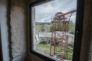 Vista desde una ventana de una gran estructura de rueda hidráulica industrial, con un edificio de piedra y vegetación al fondo.