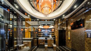 A modern hotel lobby with a central reception desk, a chandelier, and a large digital screen displaying the hotel name. - APA Hotel Hakata Ekimae 2chome (Fukuoka)