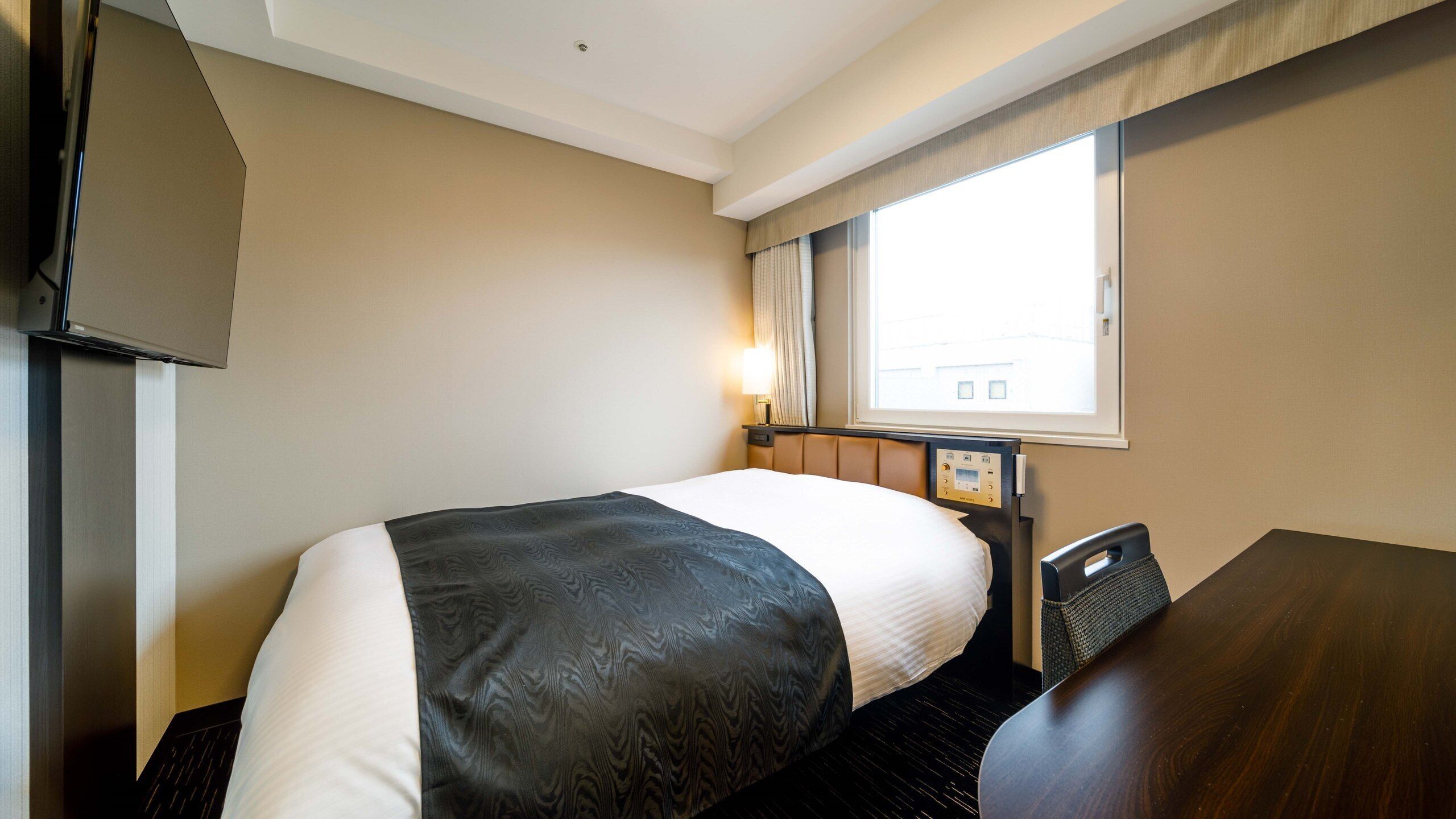 Ein Hotelzimmer mit Bett, Schreibtisch, Fernseher und einem Vorhangfenster.