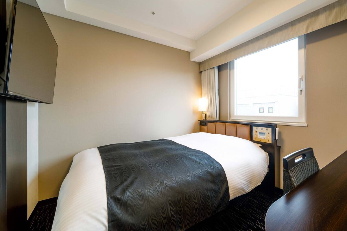 Ein Hotelzimmer mit Bett, Schreibtisch, Fernseher und einem Vorhangfenster.