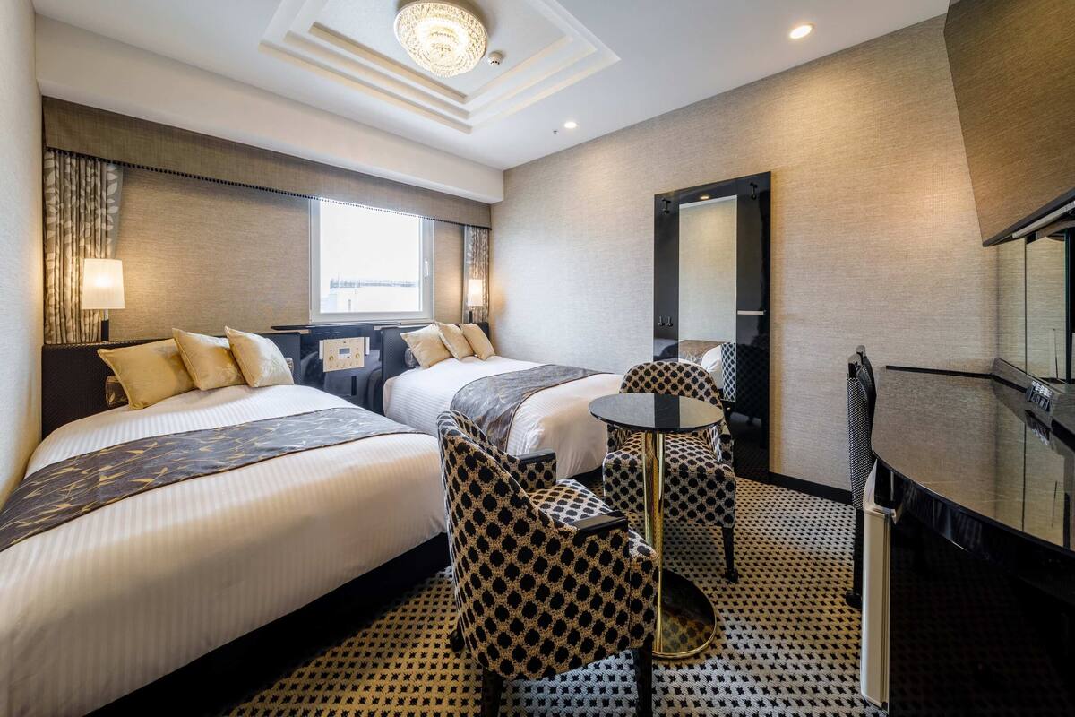Ein Hotelzimmer mit zwei Betten, einem kleinen runden Tisch, einem Spiegel und Blick ins Freie.