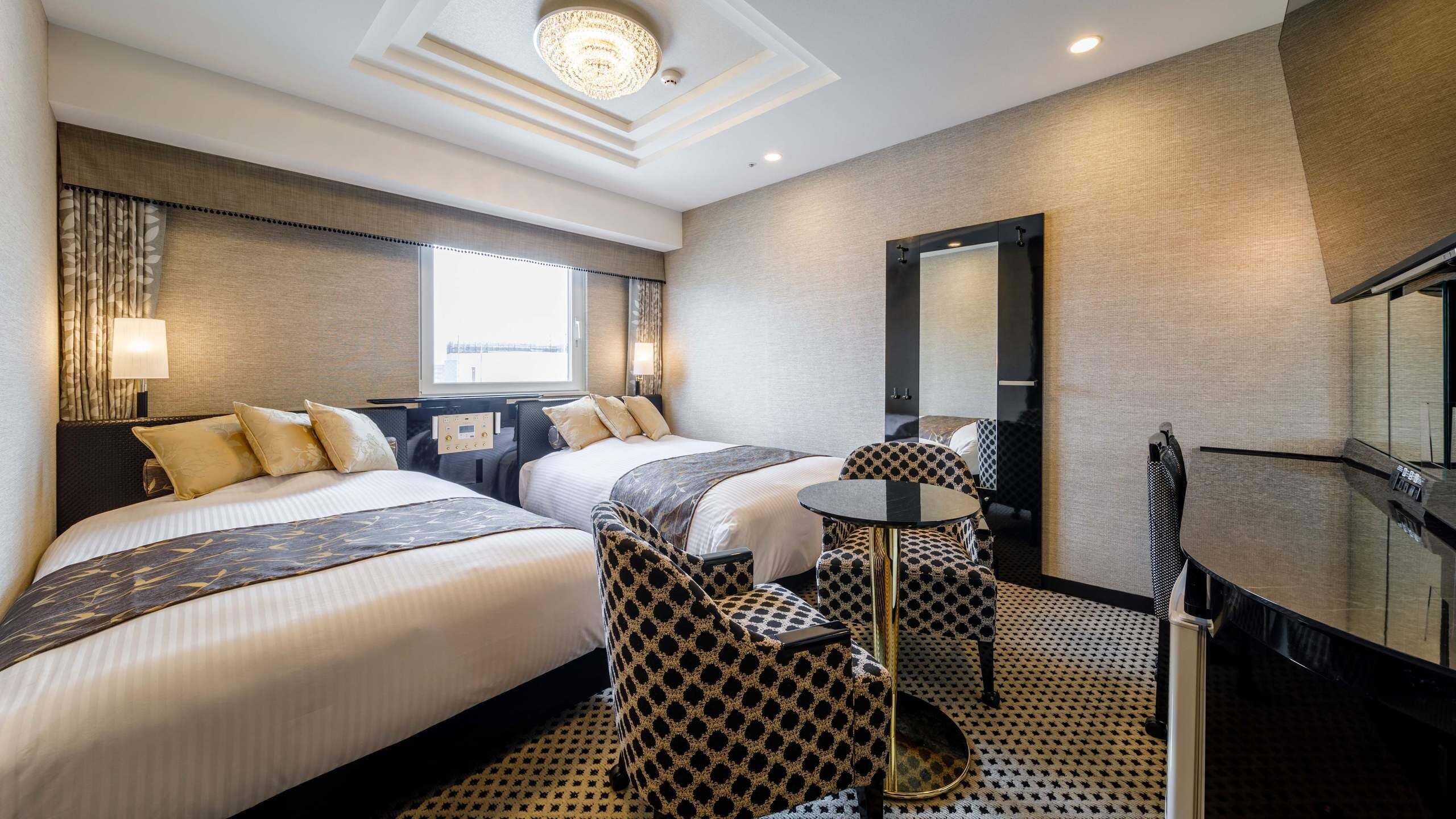 Ein Hotelzimmer mit zwei Betten, einem runden Tisch, einem Spiegel und Blick auf die Stadt.