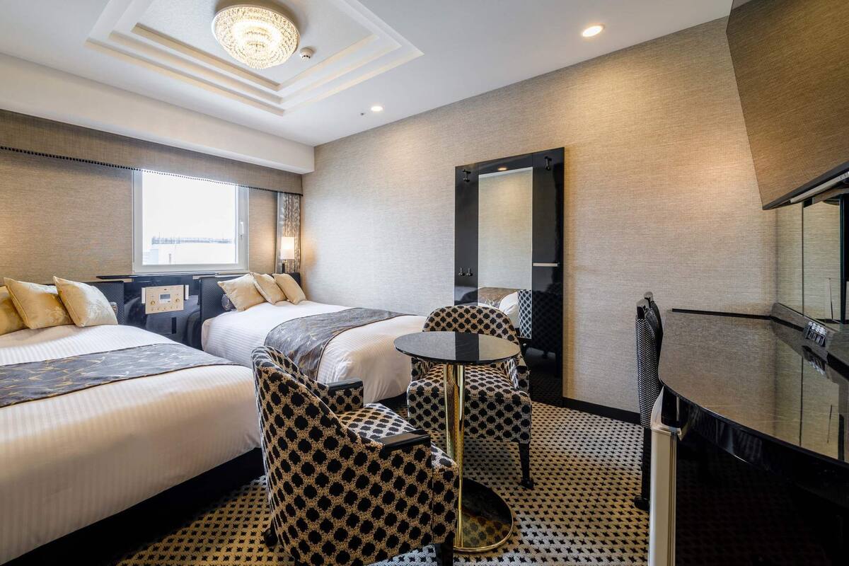 Ein Hotelzimmer mit zwei Betten, einem runden Tisch, einem Spiegel und Blick auf die Stadt.