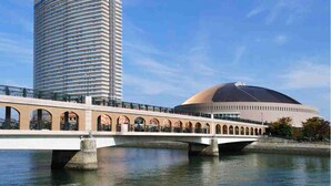 A modern building with a curved facade and a dome structure across a river. - APA Hotel Hakata Ekimae 2chome (Fukuoka)