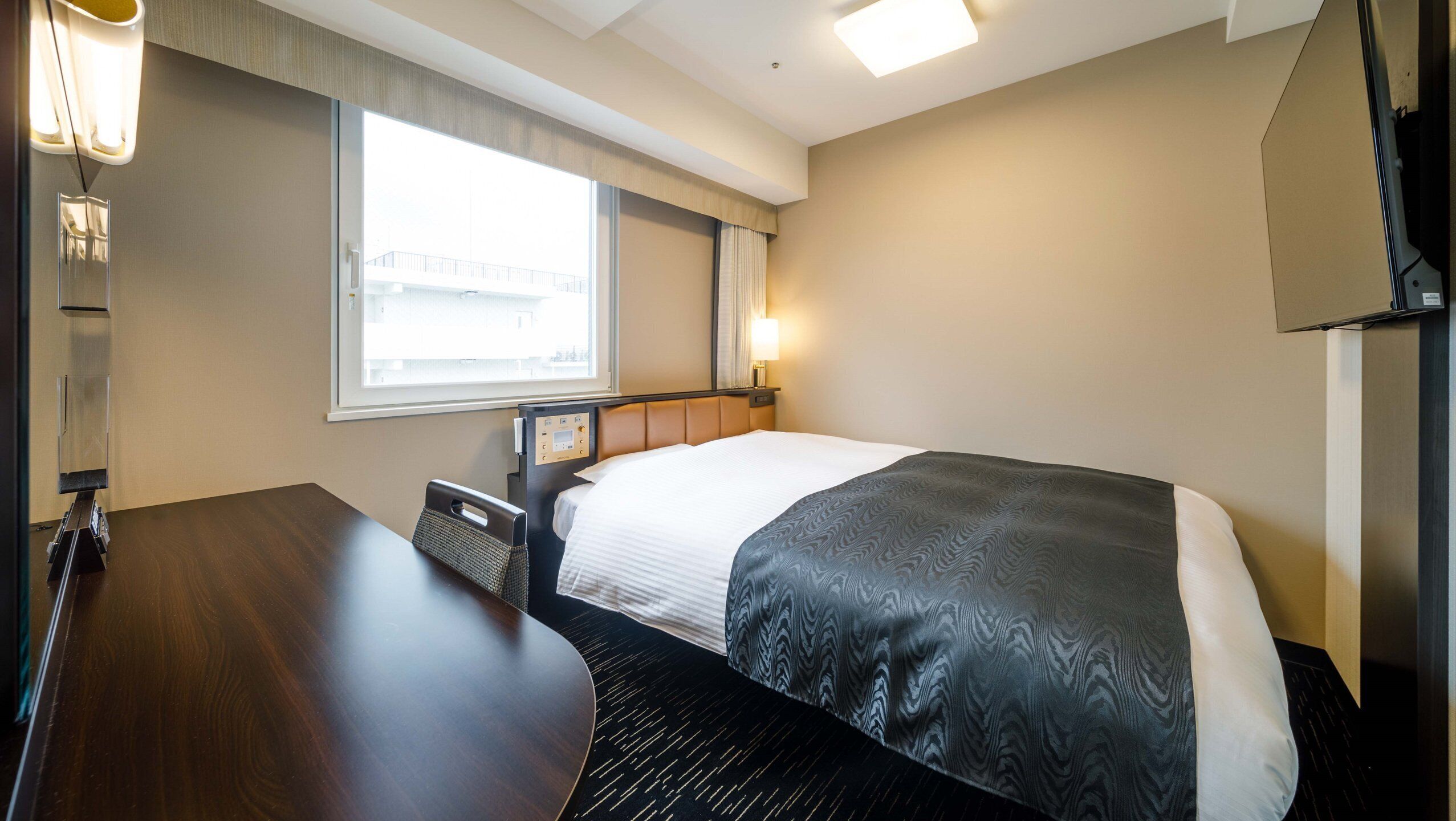 Habitación de hotel con cama, mesita de noche, lámpara, ventana y panel de control.