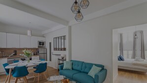 Una sala moderna con un sofá verde azulado, una mesa de centro de vidrio y una zona de comedor con sillas azules.