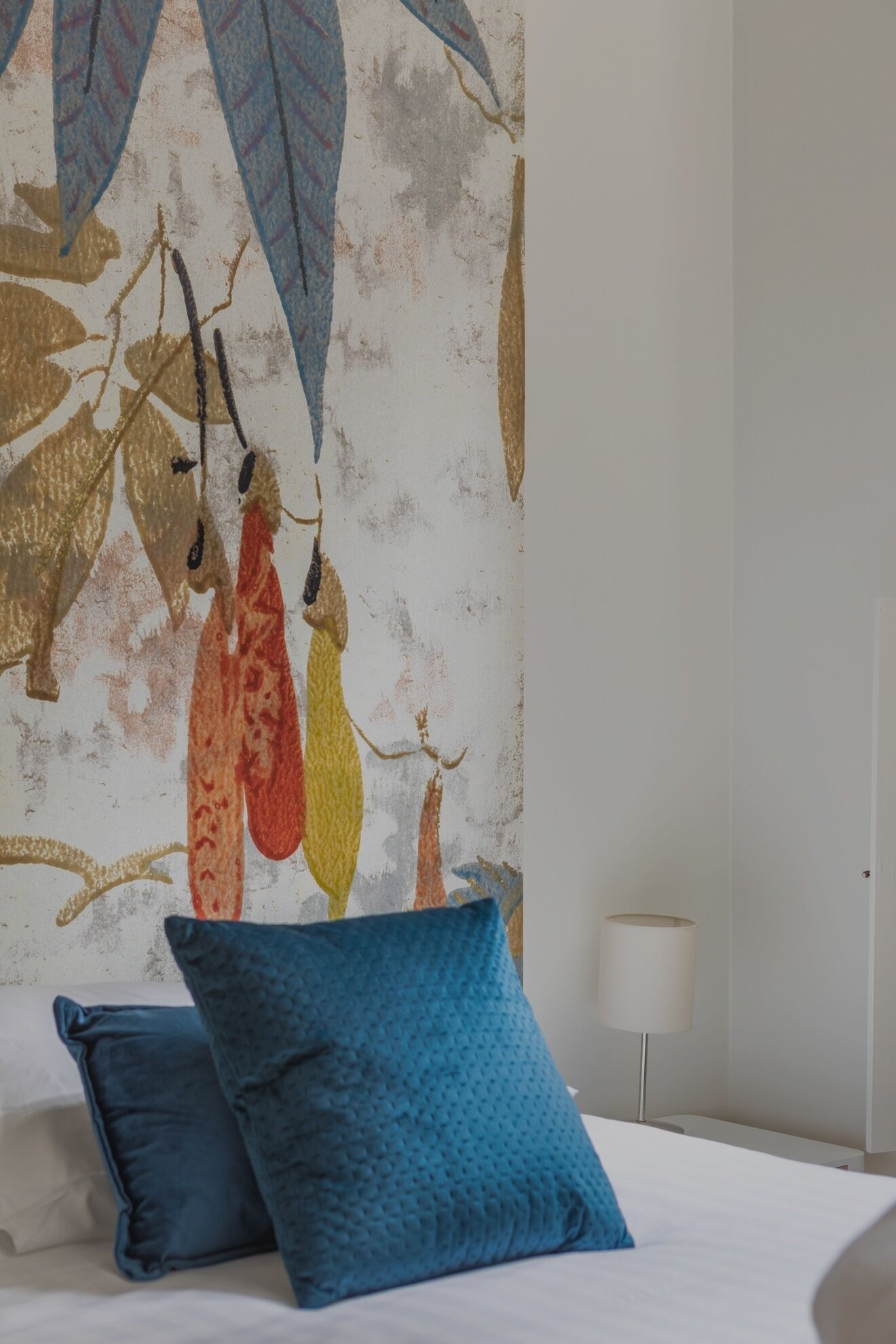 A bedroom with a bed, two blue pillows, and a wall with a leaf pattern.