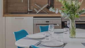 Una cocina moderna con armarios blancos, encimera de madera y una mesa de comedor con platos, vasos y un jarrón de flores.