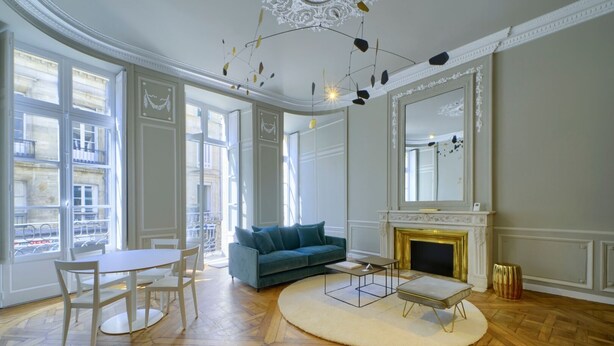 A spacious living room with a fireplace, a sofa, a dining table, and large windows.