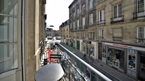 A balcony with a table and chairs, overlooking a street with shops and buildings.