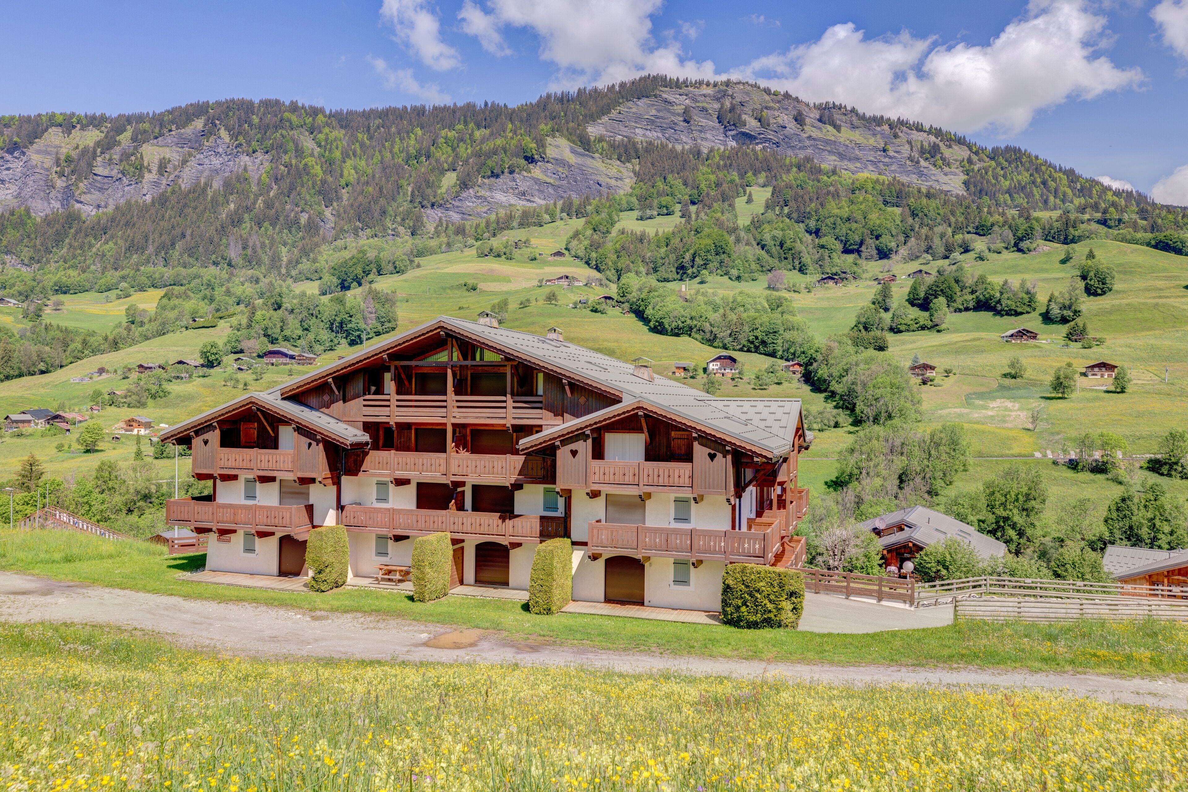 A chalet-style hotel with multiple balconies, set in a mountainous landscape with a clear sky.