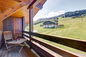 A wooden deck with a view of a mountain landscape, a wooden chair, and a table with two mugs. - L'Ecureuil - appartement familial Val d'Arly (Flumet)