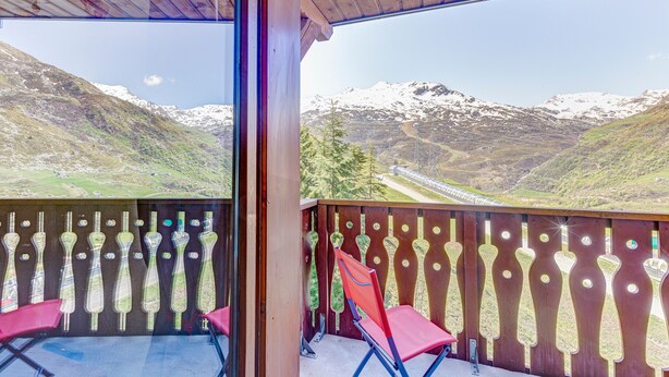 En balkon med udsigt til sneklædte bjerge, trægelændere og røde stole.