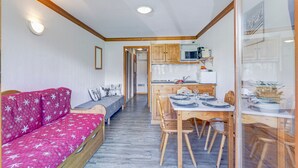 Et hyggeligt rum med en rød sofa, et træspisebord og stole. Et køkken er synligt i baggrunden.