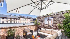 Une terrasse sur le toit, avec un mur en pierre, des meubles en osier et un grand parasol.