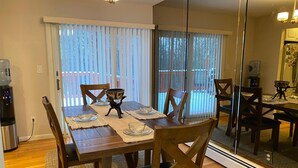 Un coin repas avec une table en bois dressée pour quatre personnes, un distributeur d’eau et une vue sur une terrasse extérieure, accessible par de grandes portes-fenêtres coulissantes.