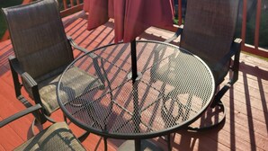 Une terrasse avec une table ronde et deux chaises, un parasol rouge et une rambarde.