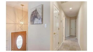 Un couloir avec une porte en bois, un luminaire aux formes géométriques et un tableau représentant un cheval accroché au mur.