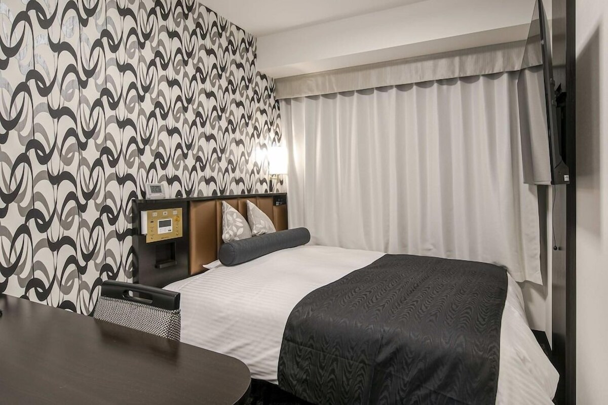 Une chambre d’hôtel avec un lit, un bureau, une chaise, une télévision et une fenêtre avec des rideaux.
