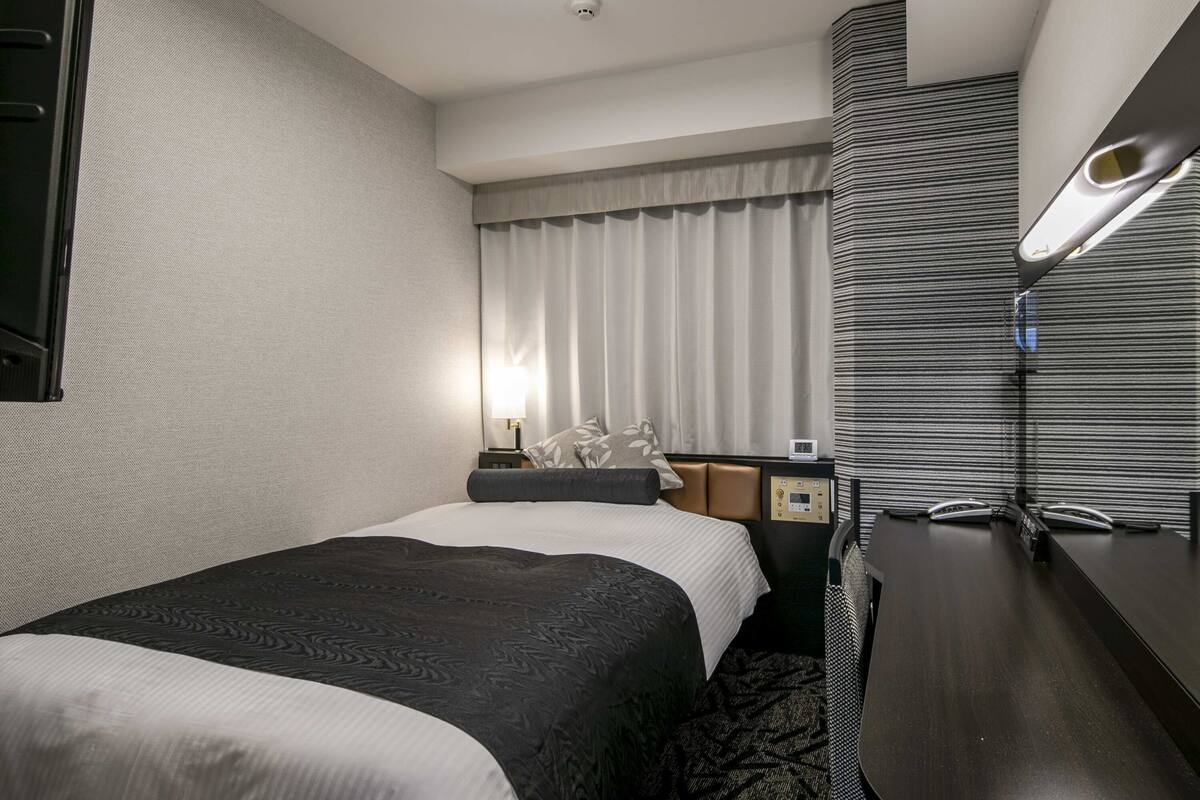 Ein Hotelzimmer mit zwei Betten, einem Schreibtisch, einer Lampe, einer Uhr und einem Fenster mit Vorhängen.