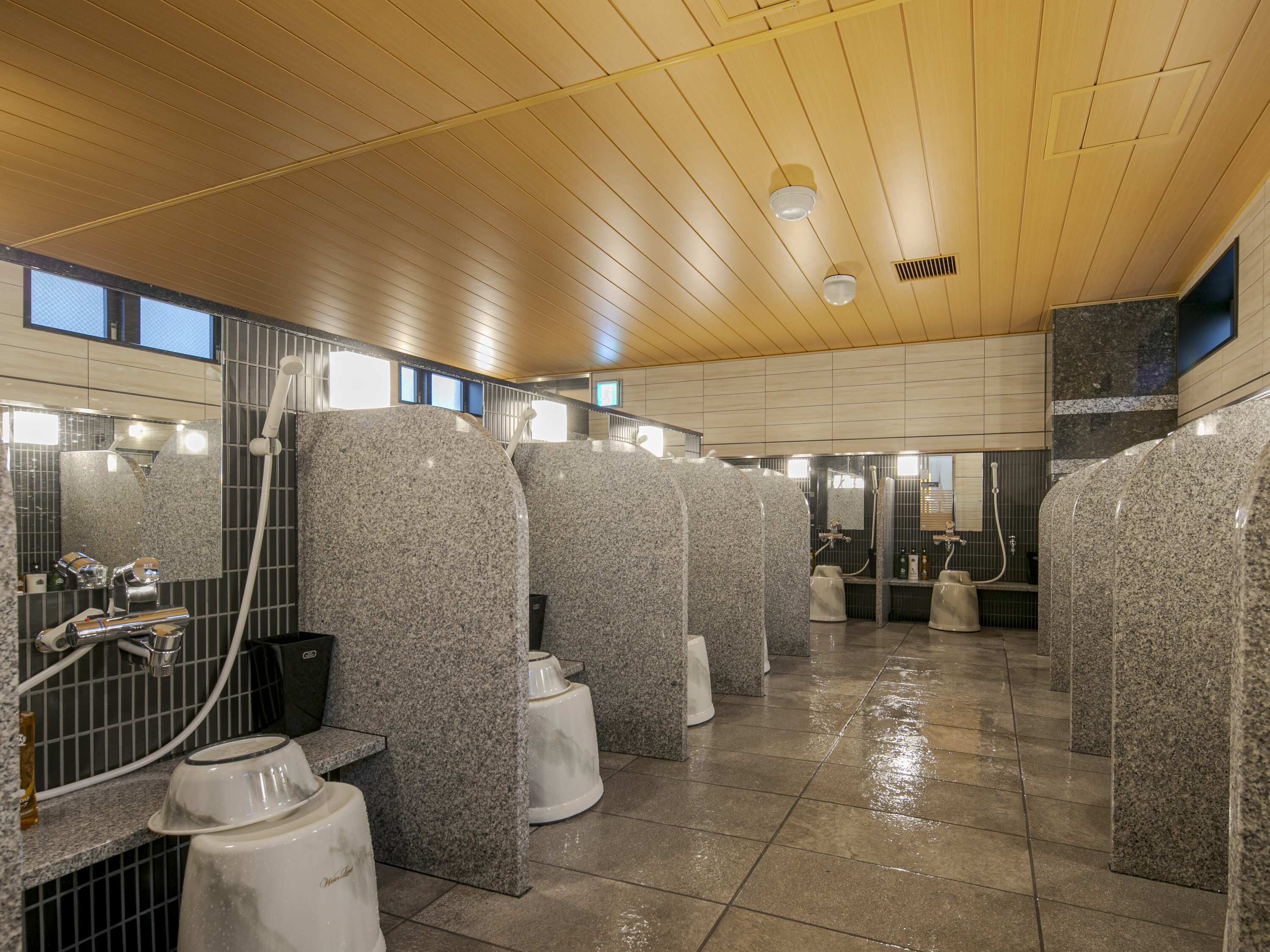 A public restroom with granite counters, a wooden ceiling, and a tiled floor.