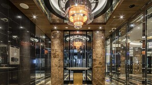 Un hall d’hôtel moderne, agrémenté d’un imposant lustre, de colonnes en marbre et d’un ascenseur en verre.