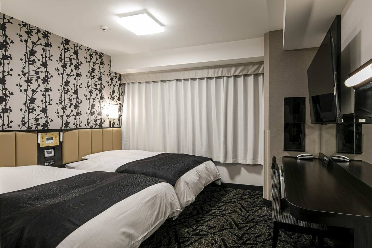 Ein Hotelzimmer mit zwei Betten, einem Schreibtisch, einem Fernseher und einer Steuerung.