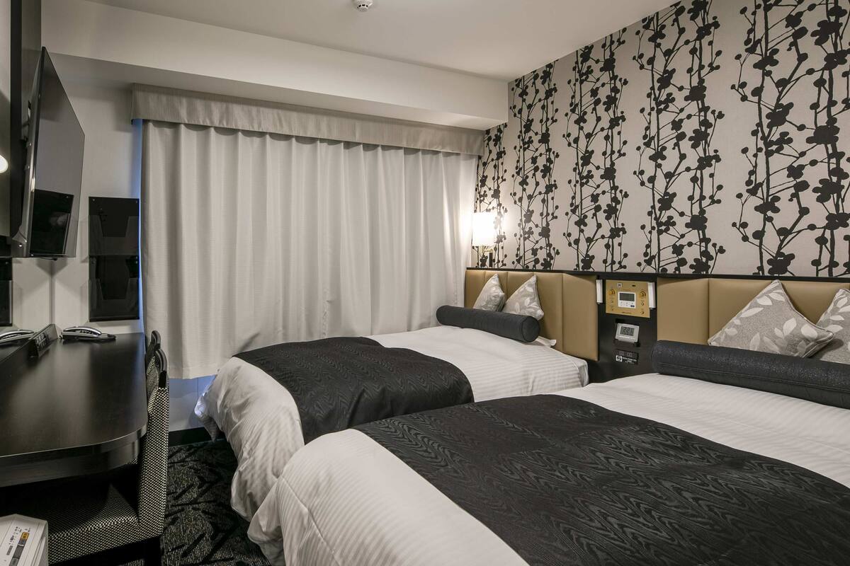 Ein Hotelzimmer mit zwei Betten, einem Schreibtisch mit Telefon, einem Fernseher und einer Wanduhr.