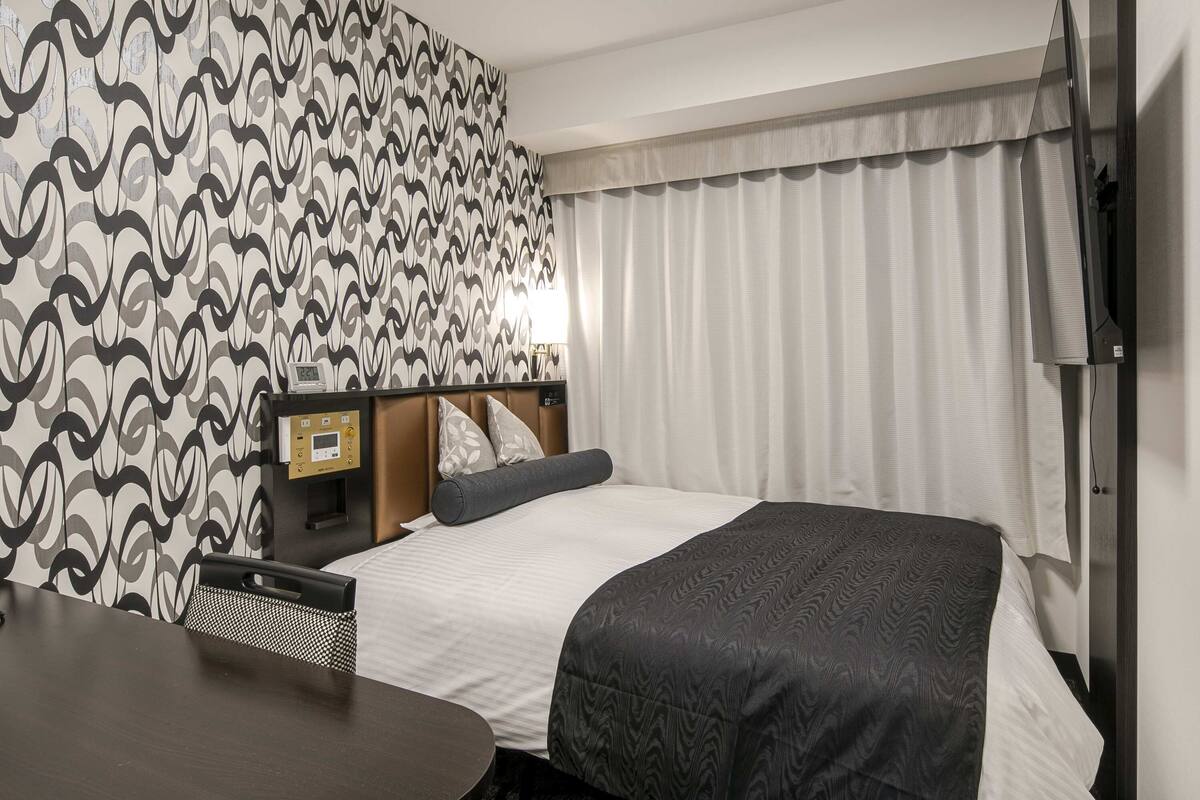 Ein Hotelzimmer mit Bett, Schreibtisch, Stuhl, Fernseher und einem Fenster mit Vorhängen.