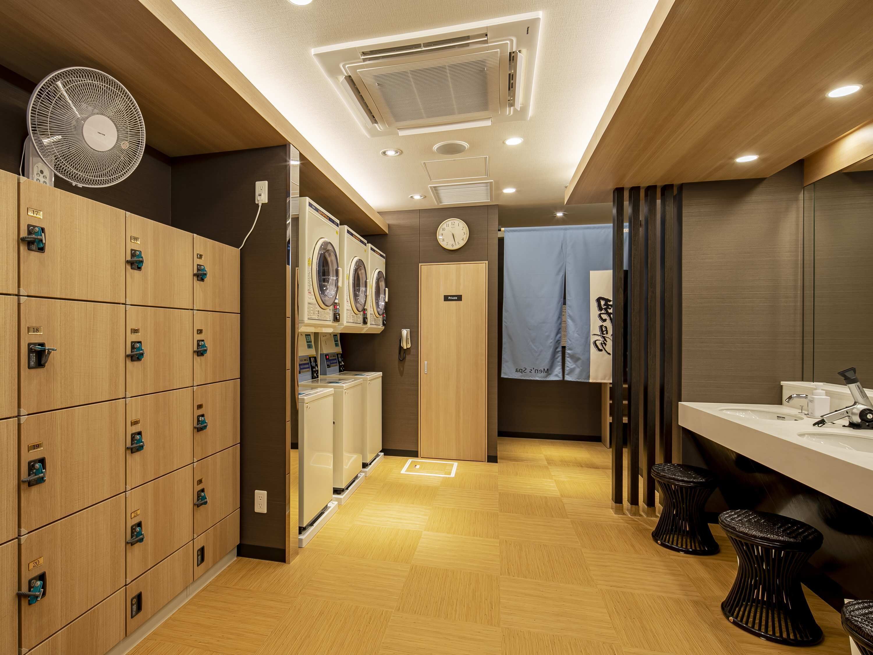 Een hotelbadkamer met houten kasten, een wasmachine, een spiegel en een wastafel.