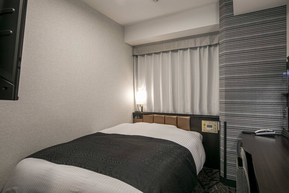 Ein Hotelzimmer mit Bett, Schreibtisch, Lampe und einem fenster mit Vorhängen.