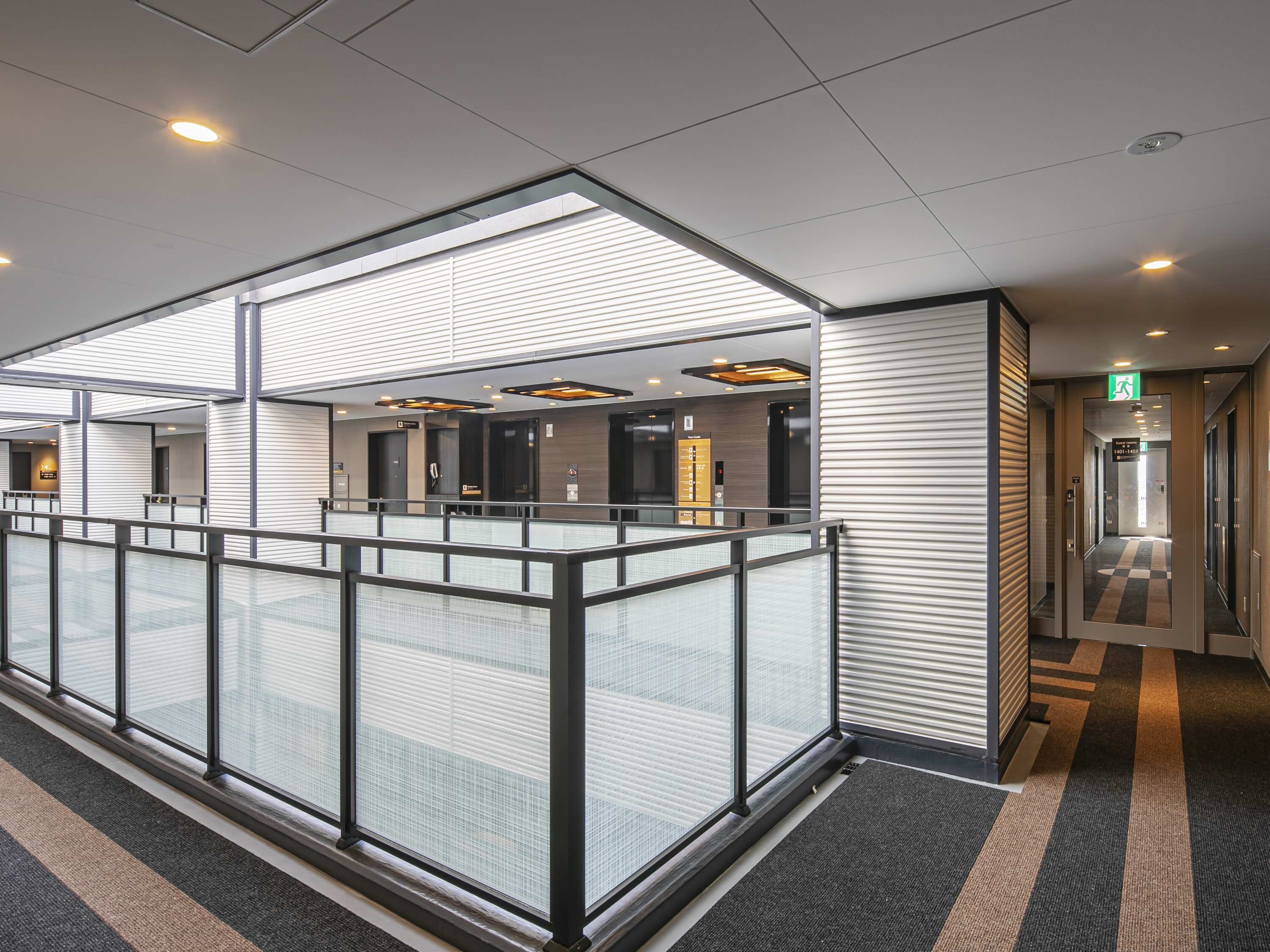 A modern hotel lobby with a glass partition, elevators, and a check-in area.