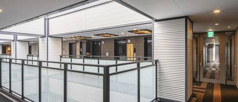 A modern hotel lobby with a glass partition, elevators, and a check-in area.