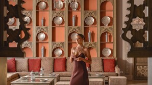 A woman in a room with a large, ornate chandelier, a sofa set, and a wall with decorative plates. - JAZ Tamerina, Almaza Bay (Marsa Matrouh)