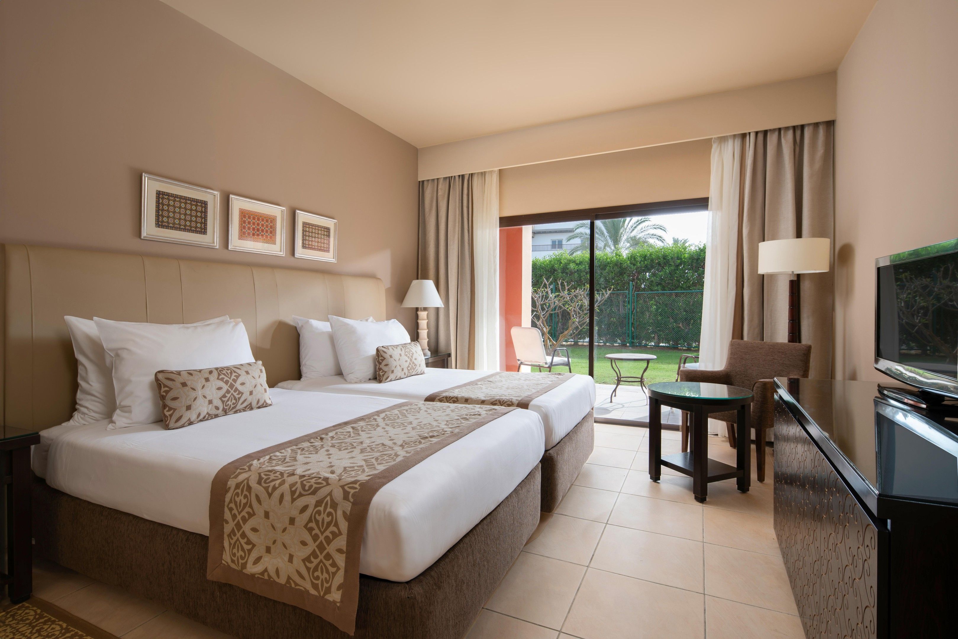 Habitación de hotel con dos camas, televisión, escritorio y vista al exterior.