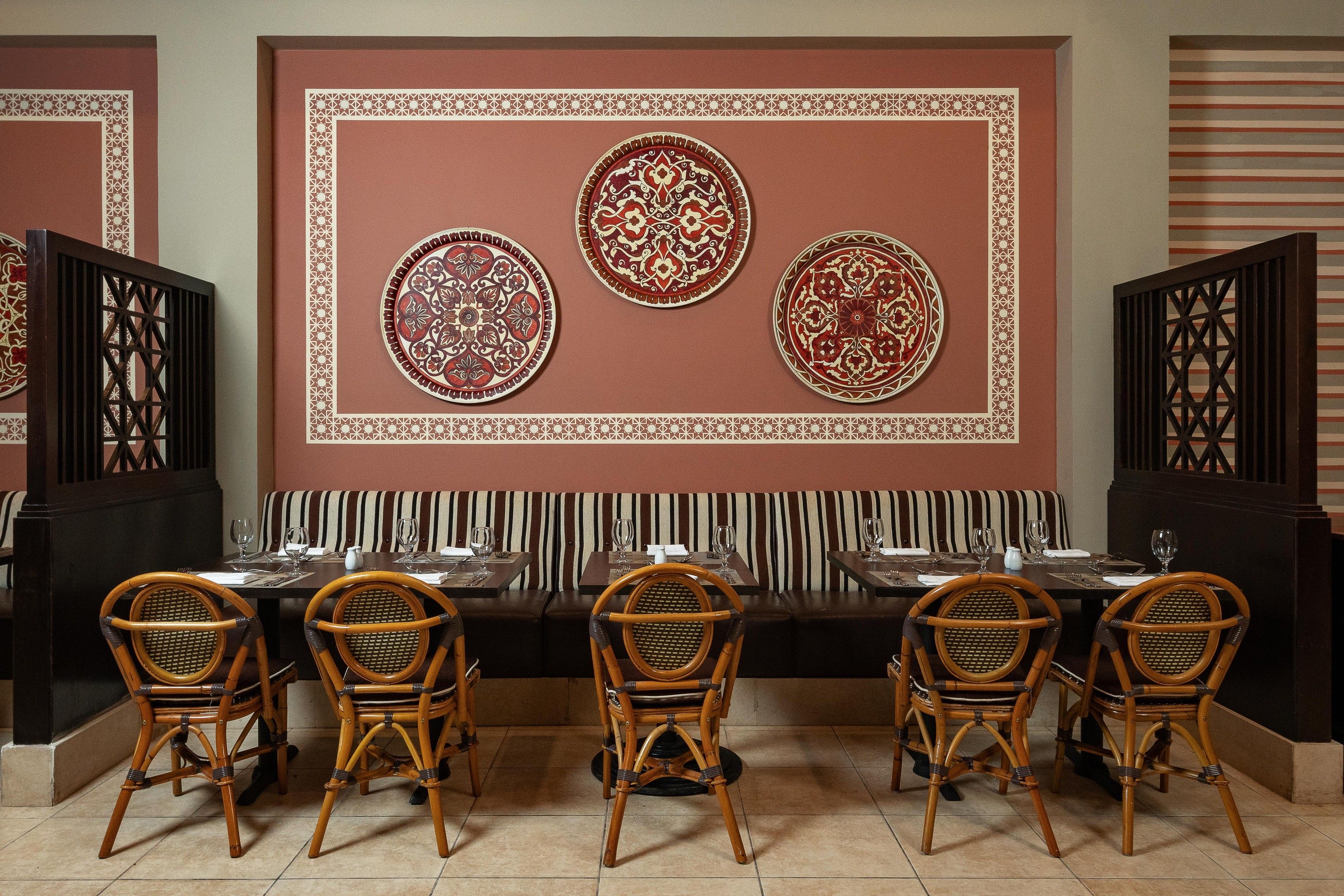 A restaurant interior with a long dining table, striped cushioned bench, and decorative wall panels.