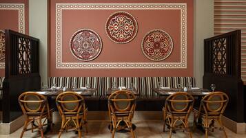 A restaurant interior with a long dining table, striped cushioned bench, and decorative wall panels.