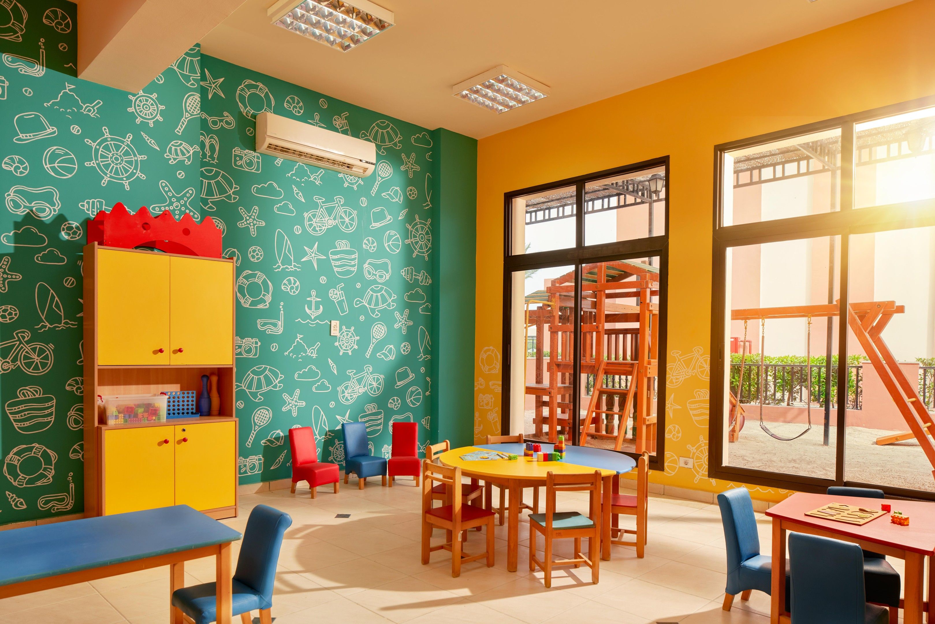 Ein Spielzimmer für Kinder mit bunten Wänden, einem Spieltisch und einem großen Fenster.